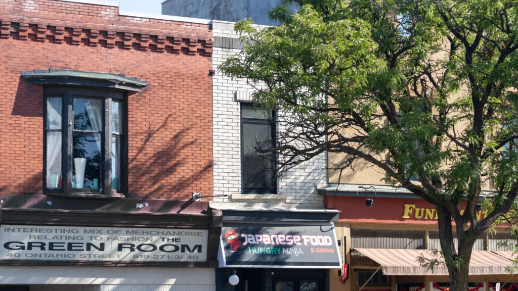 Edison Stratford | Krista the Explorer Street view of storefronts on a sunny city block.