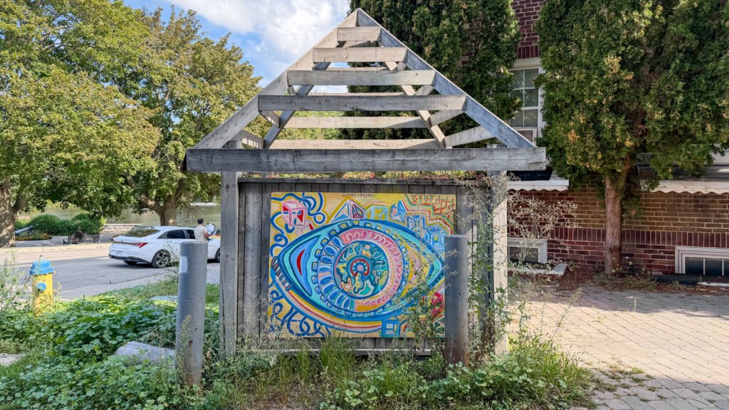 Street Art Stratford | Krista the Explorer Street art in city on wooden sign next to road.