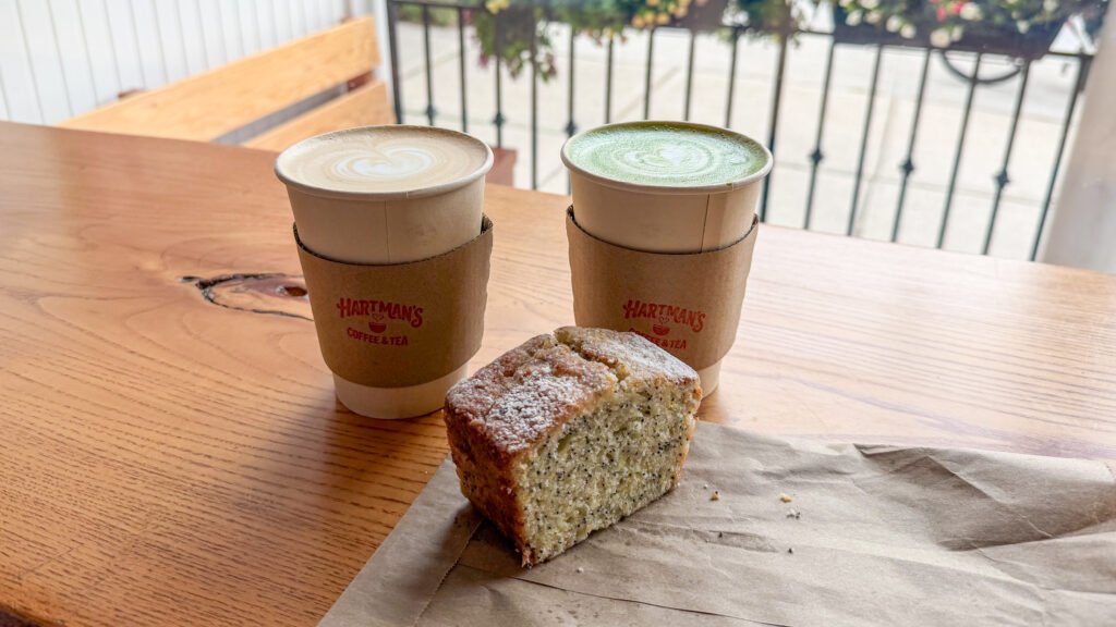 Cafe Stratford | Krista the Explorer Two paper cups of coffee with latte art sit on a wooden table, with a slice of lemon loaf in front.