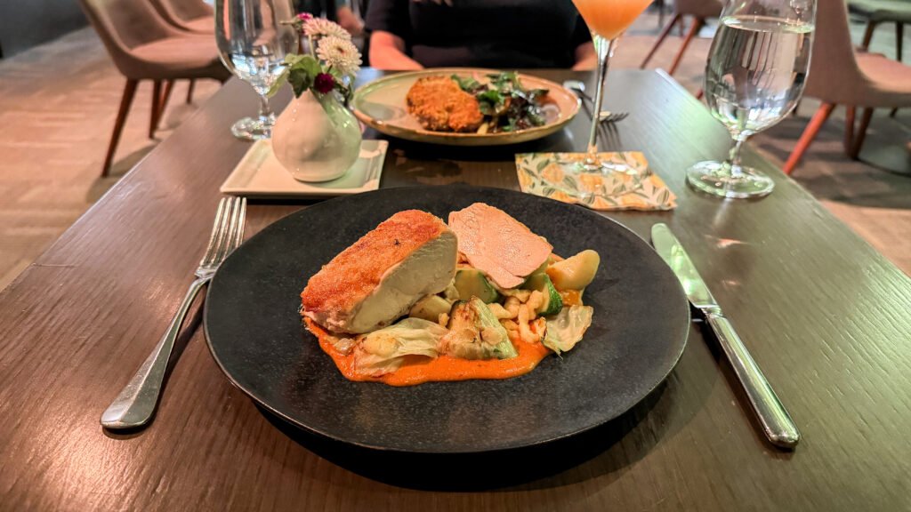 The Prune Stratford | Krista the Explorer Black plate with chicken breast and veggies in an orange sauce.