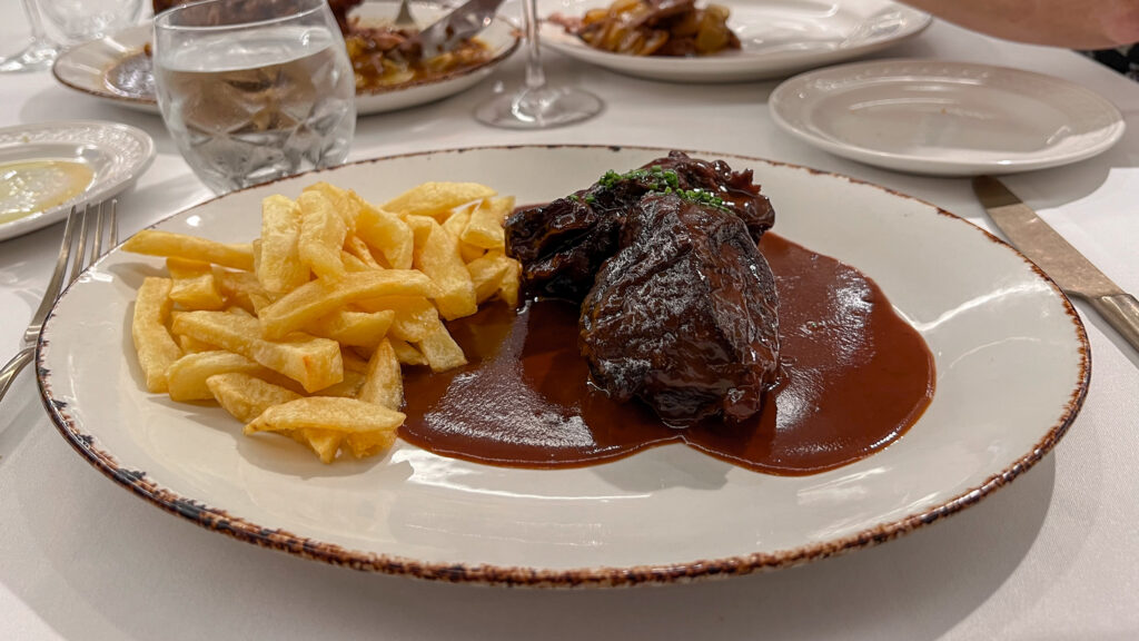 Braised beef in dark sauce with a side of thick-cut fries on a white plate.