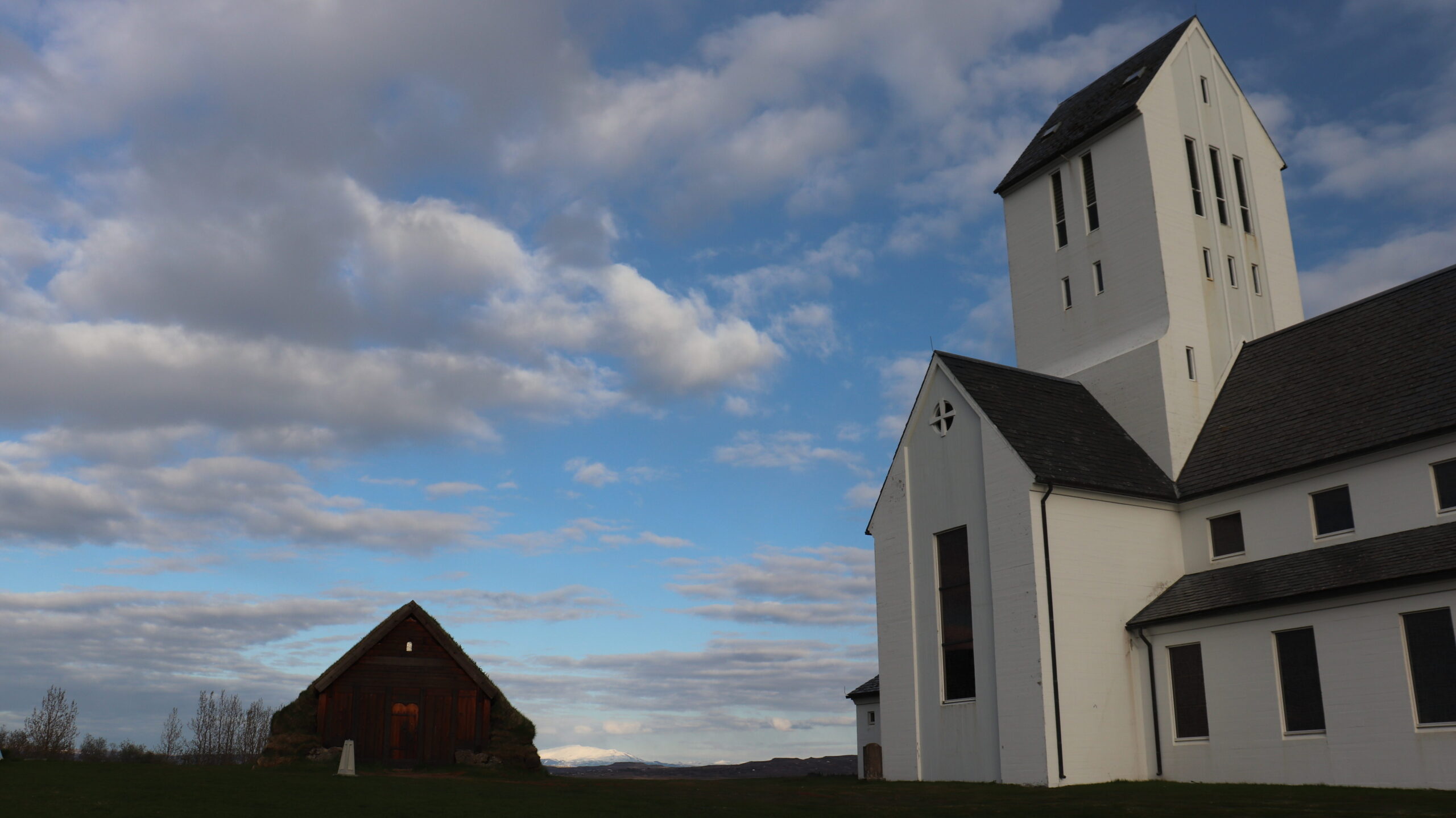 White Icelandic church next to wooden hut.