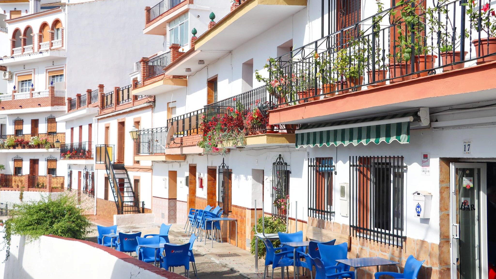 Line of white buildings with blue chairs in front.