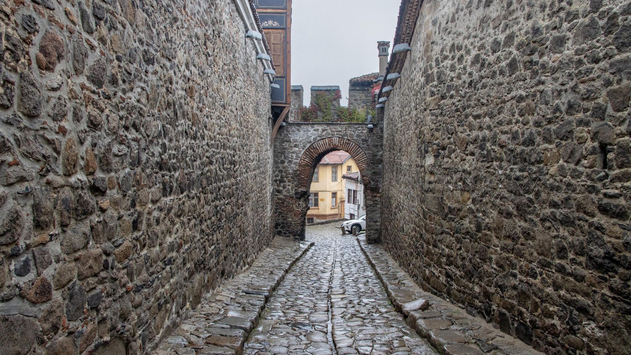 Cobbled street with stone walls and arch.