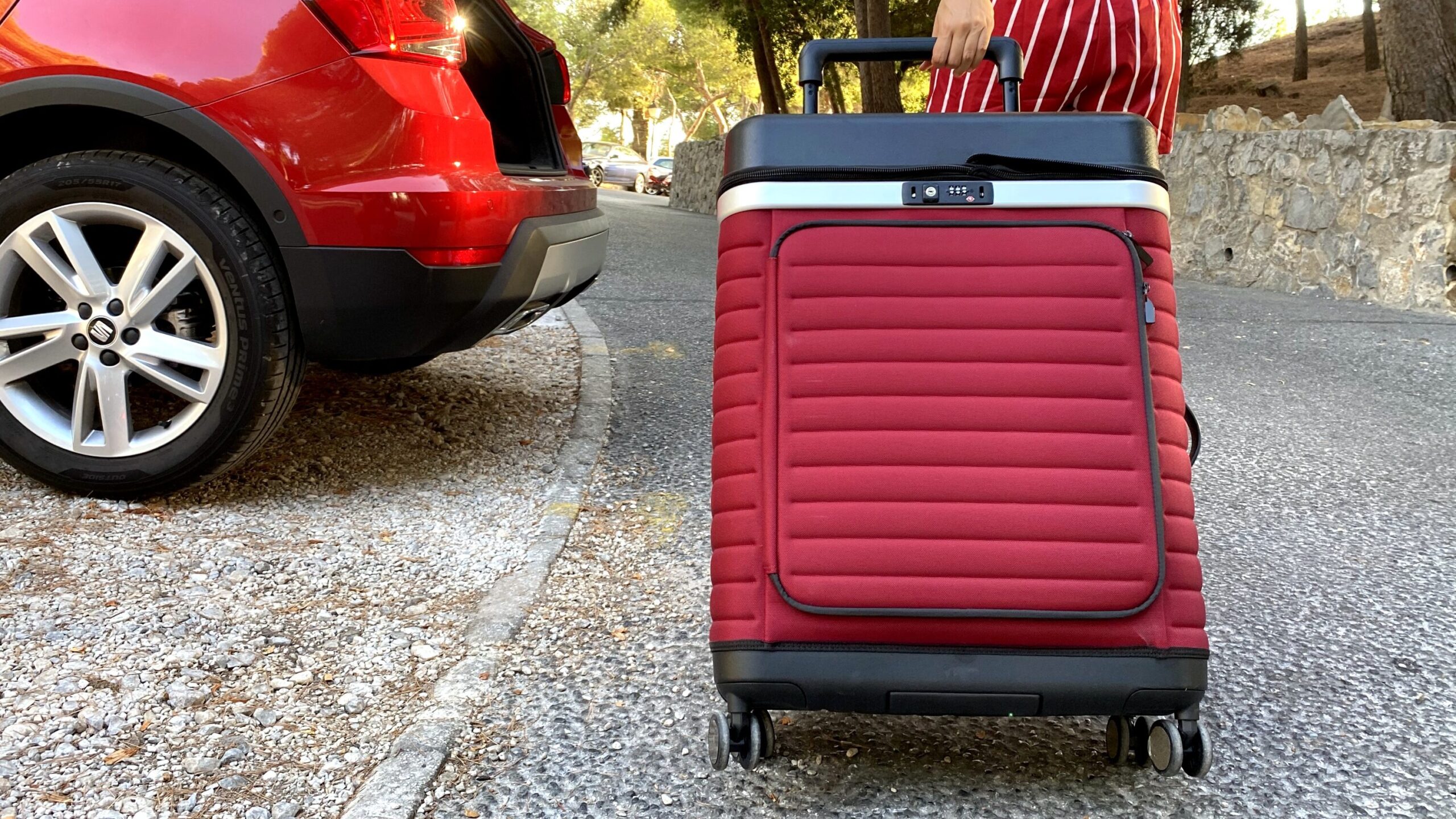 Red and black suitcase being pulled on two wheels.