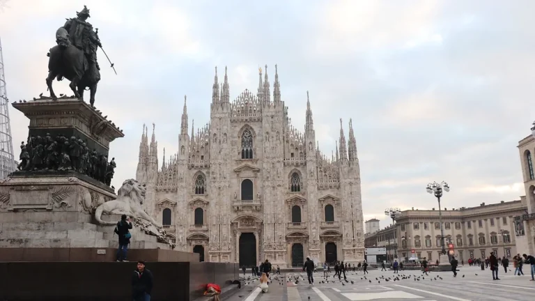 Large cathedral in Milan with statue in plaza.