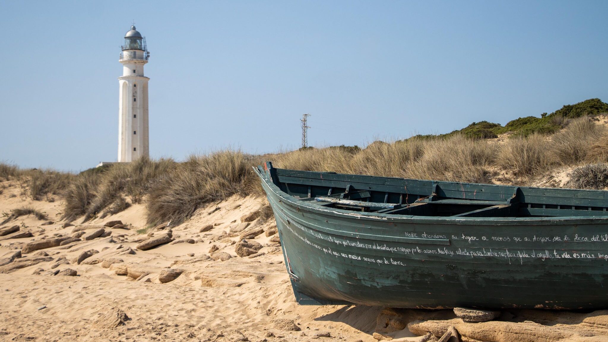 Wooden boat sitting on beach next to lighthouse.