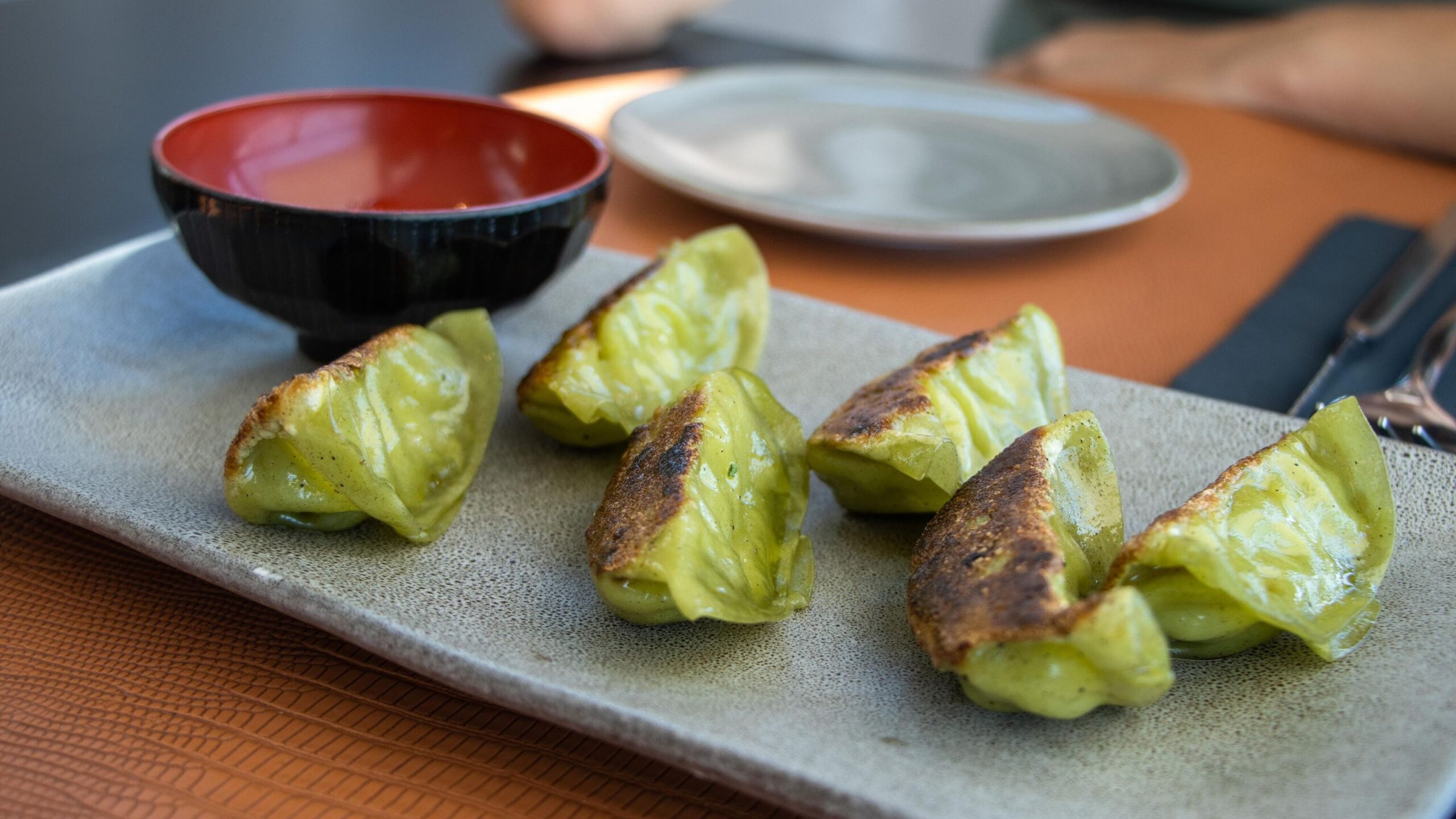 Green gyozas served with soy sauce.