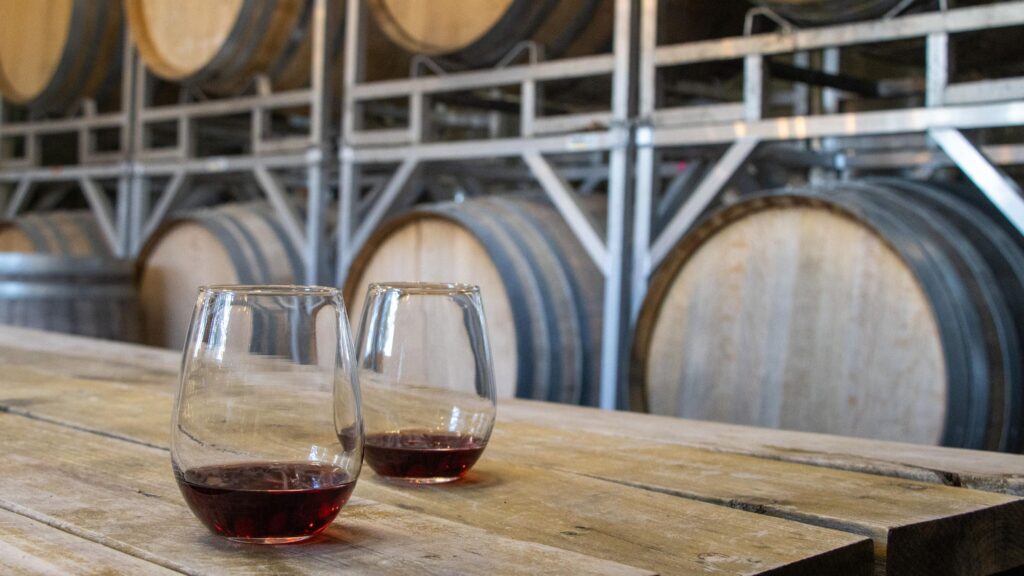 Two glasses of wine next to wine barrels.