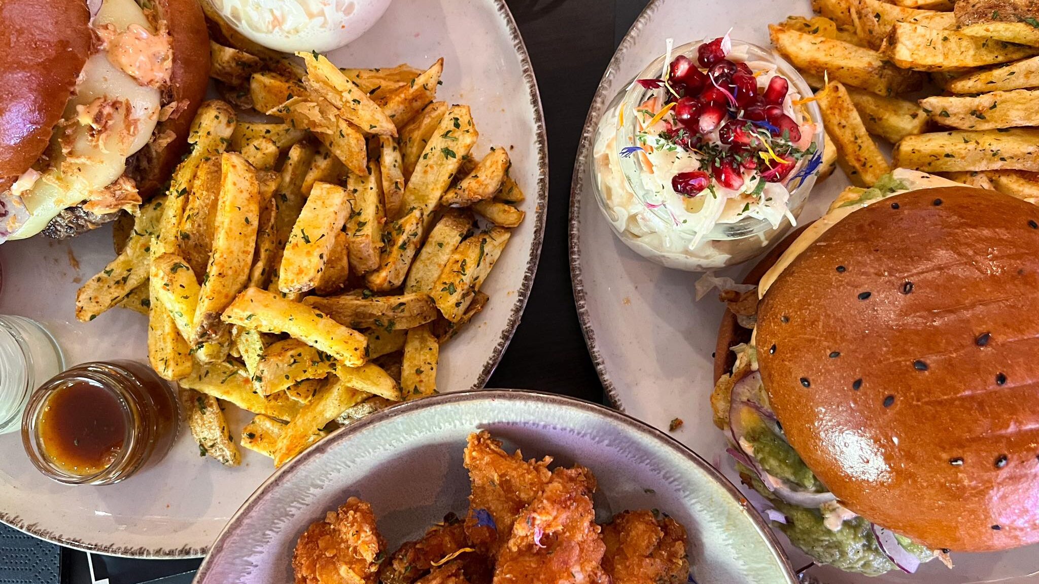 Burgers and fries with sides on table.