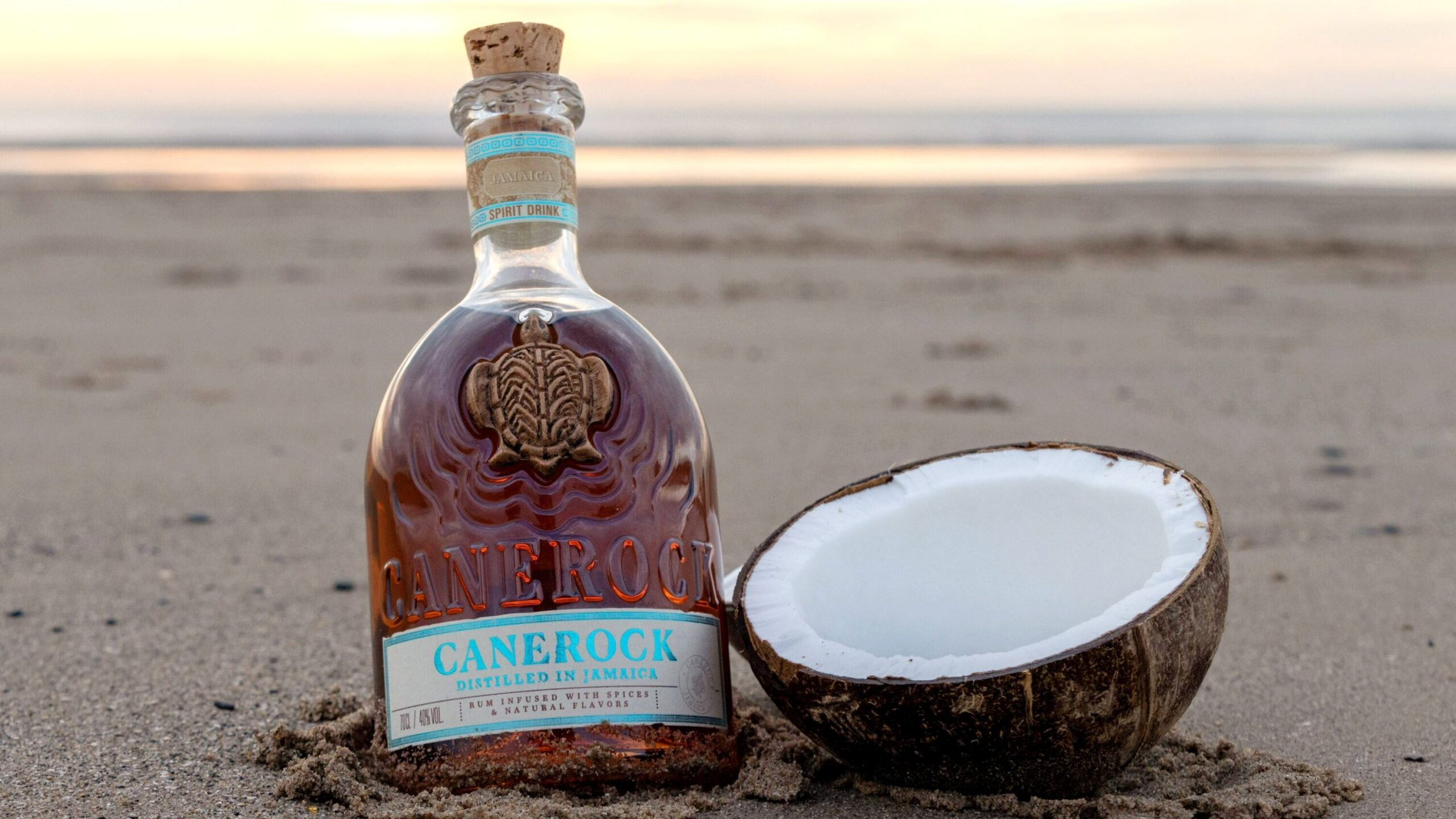 Bottle of rum next to coconut on beach.