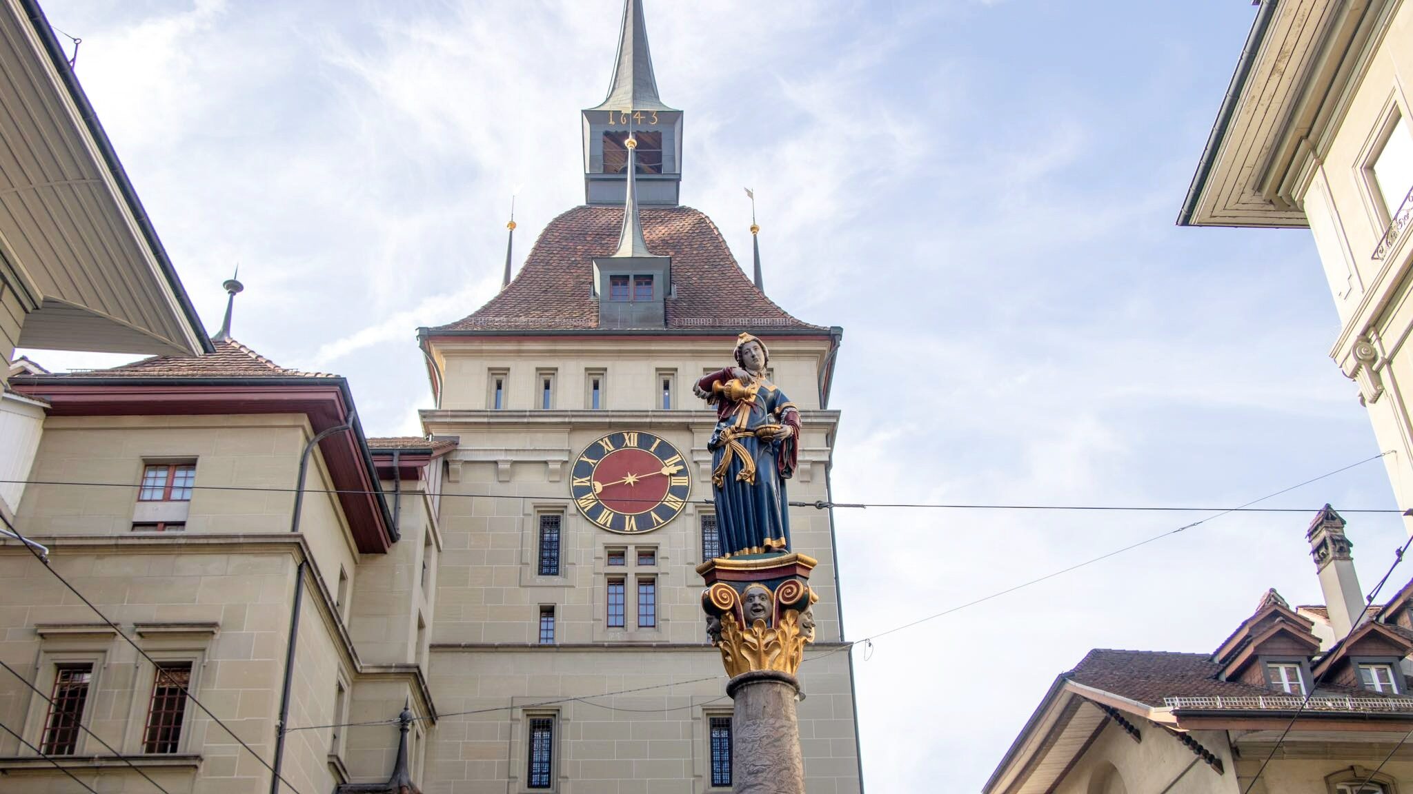 Medieval clock tower and gate with fountain in front.