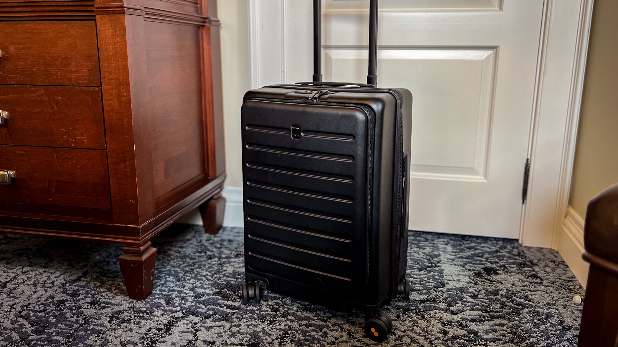 Black hard shell suitcase in front of hotel room door.