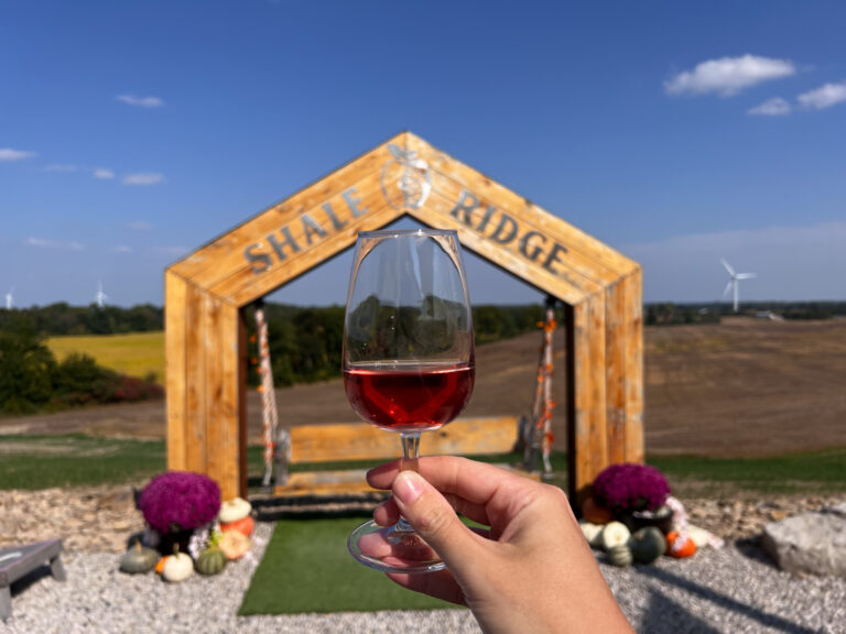 Red wine held up in front of winery sign unique Ontario experiences.