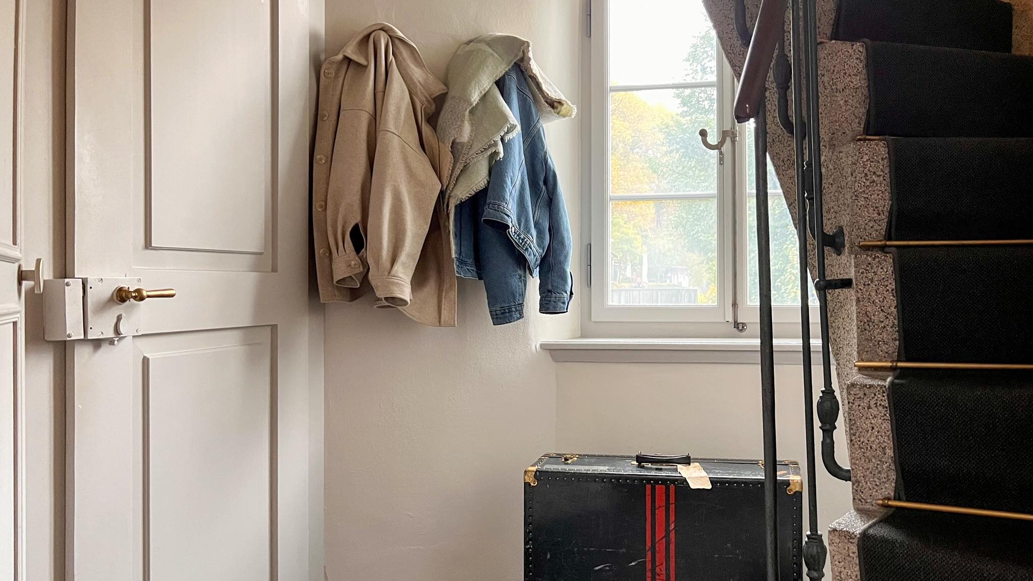 Spiral staircase next to window with coats hung on wall.