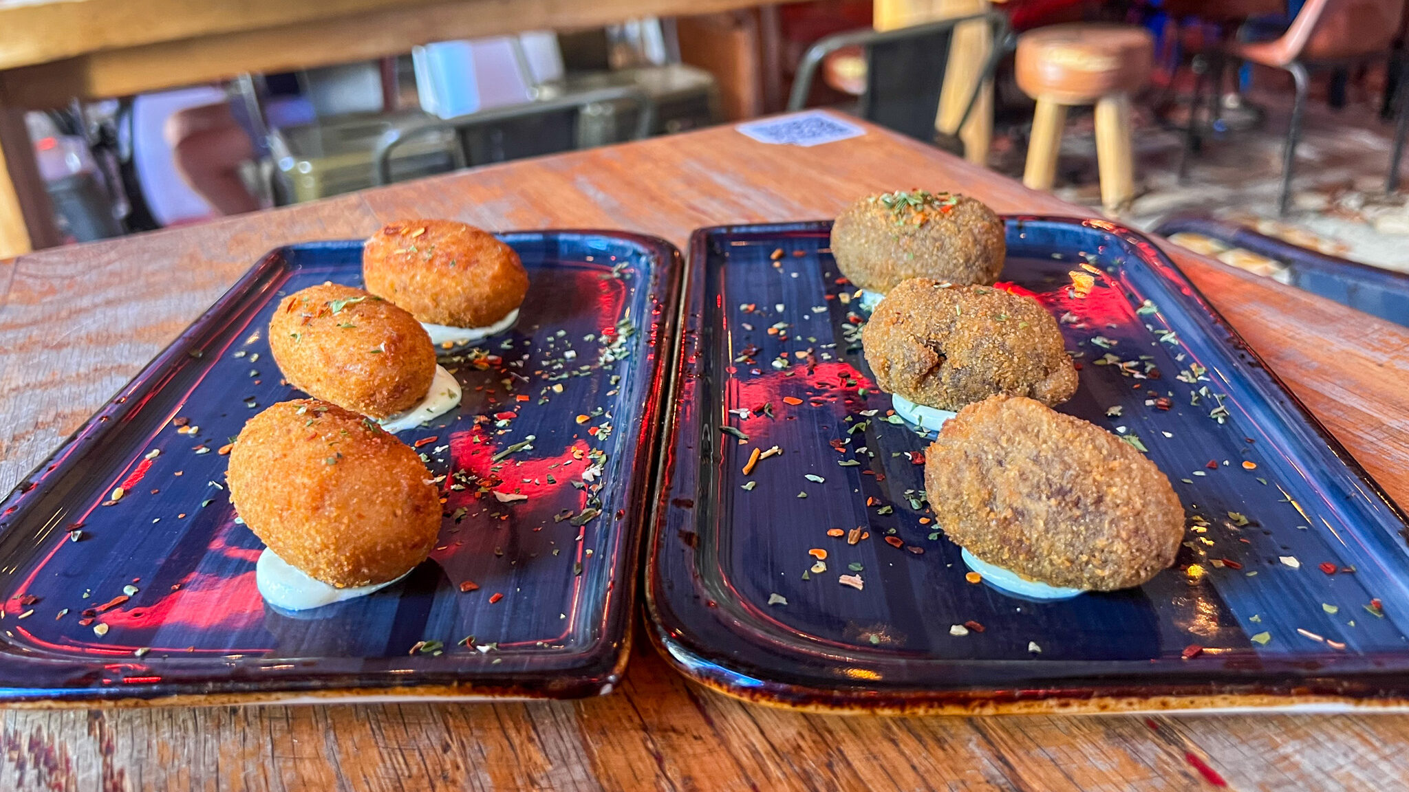 Two plates of croquettes sitting on sauce.