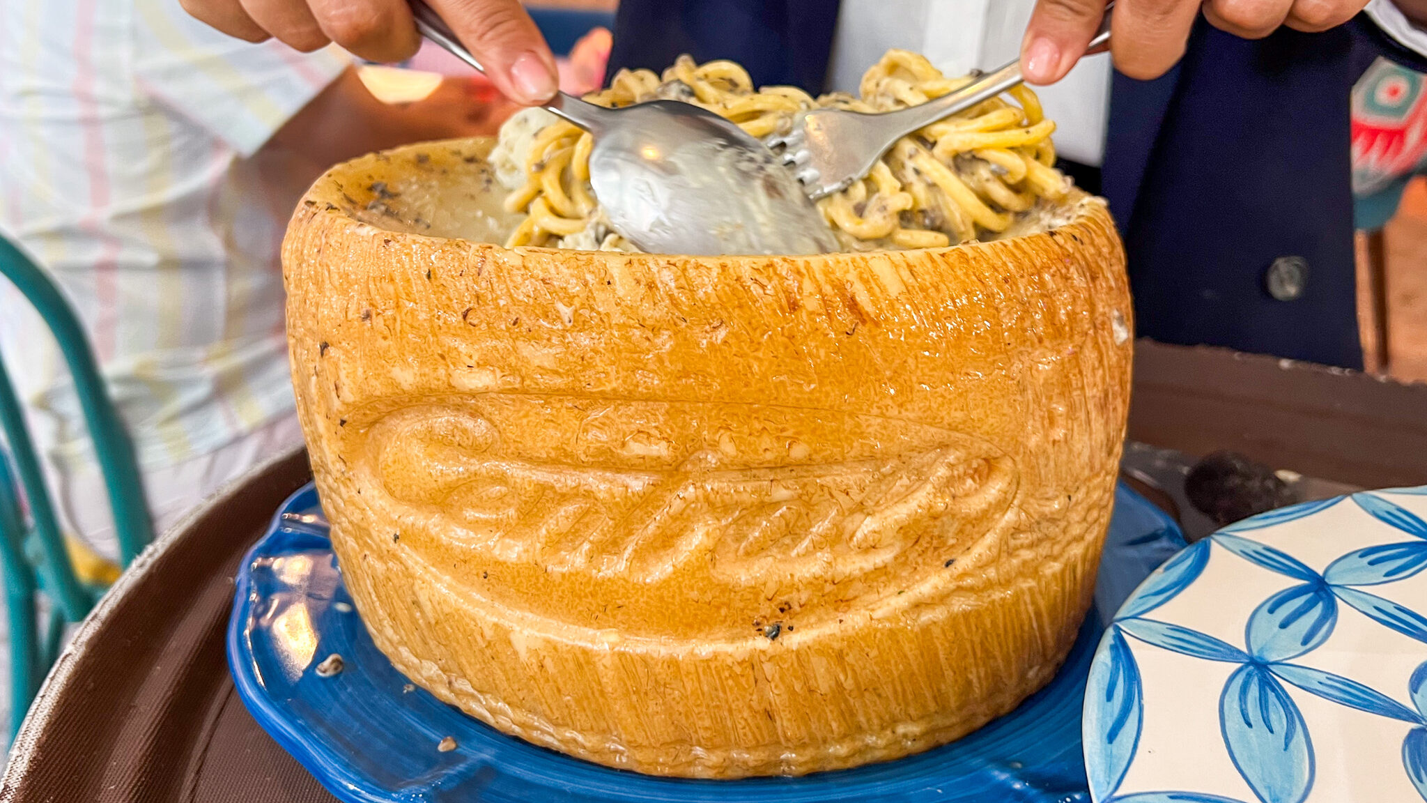 Large cheese wheel with pasta being mixed in.