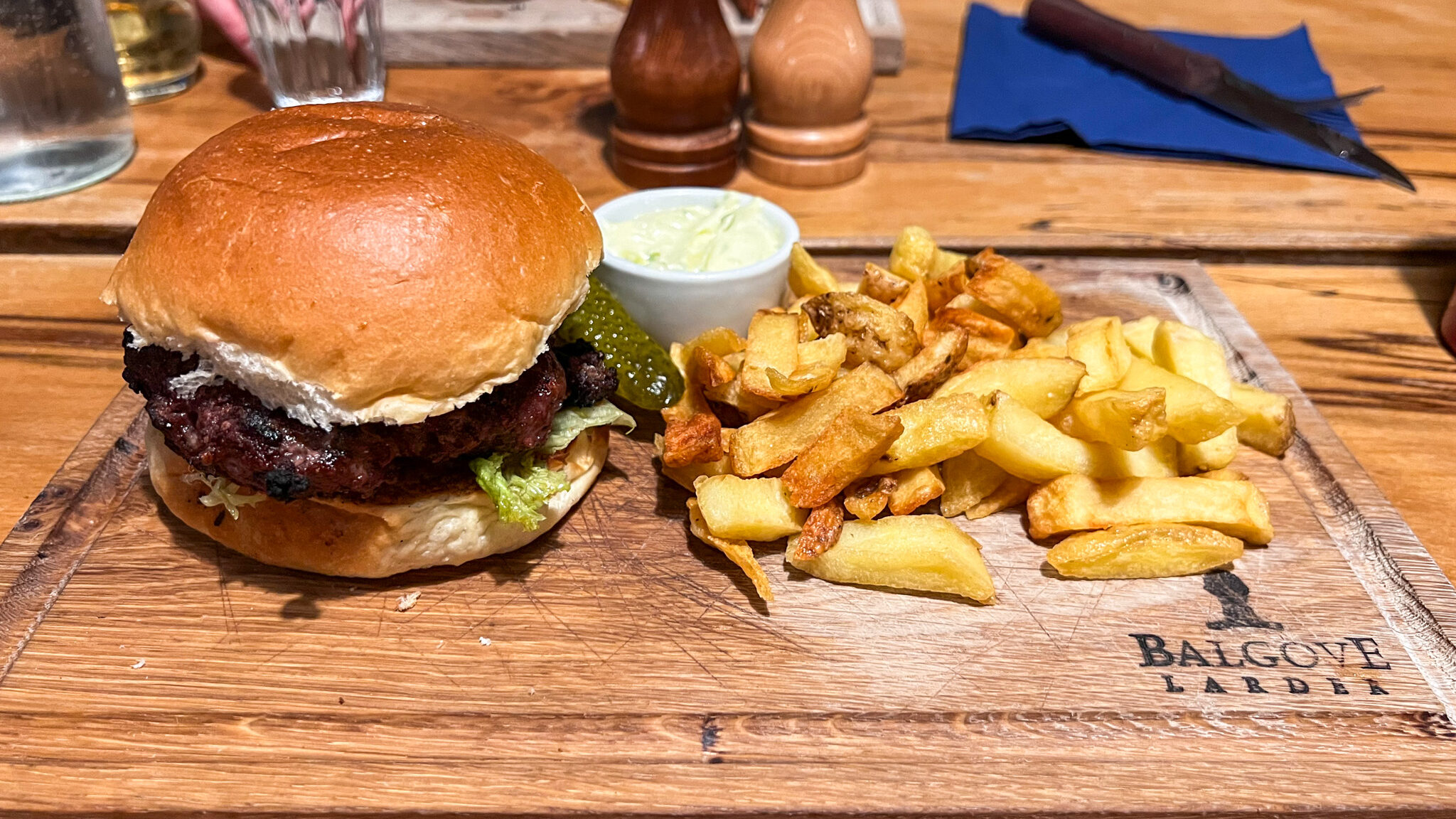 Beef burger with fries served on wooden board.