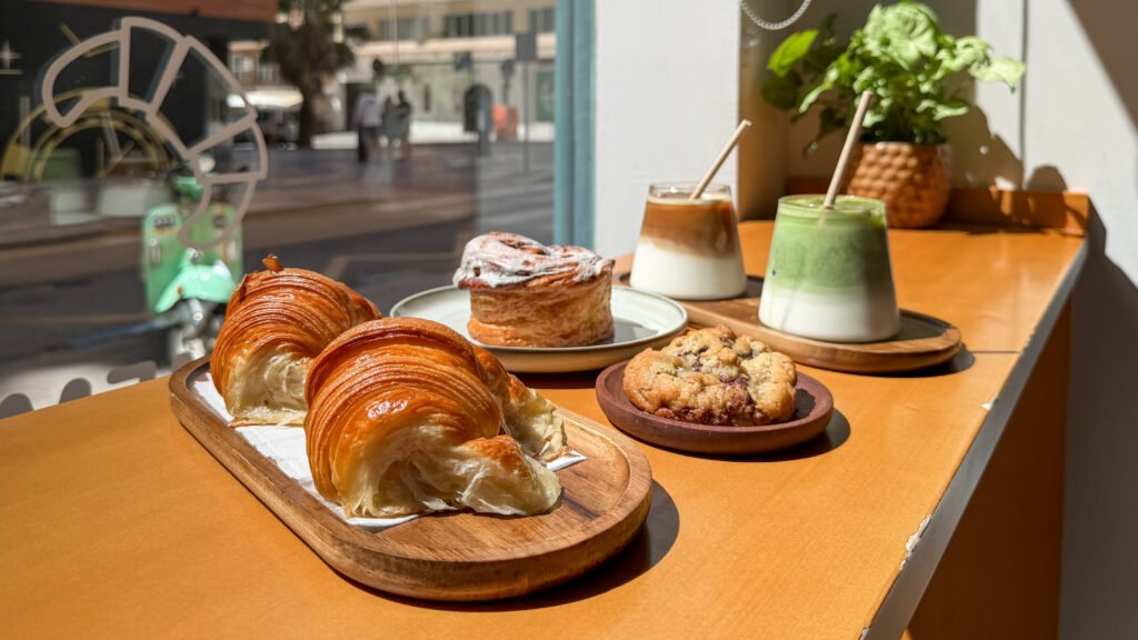 Fluffy croissants on wooden plate with iced drinks behind.