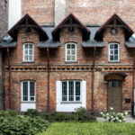 Small brick house among larger buildings.