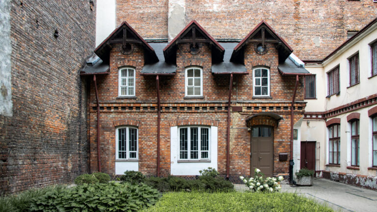 Small brick house among larger buildings.