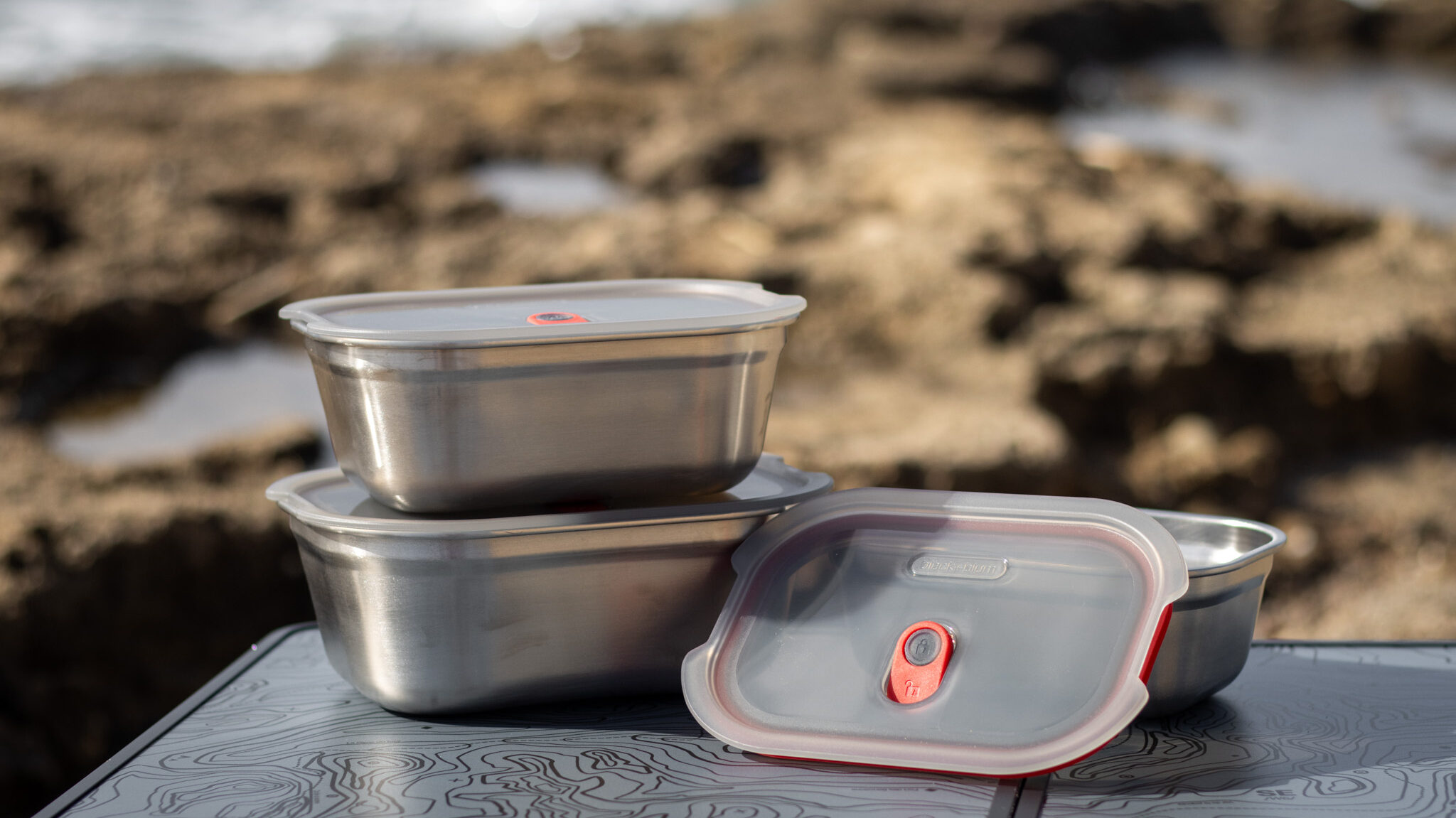 Three sizes of reusable food containers on beach.