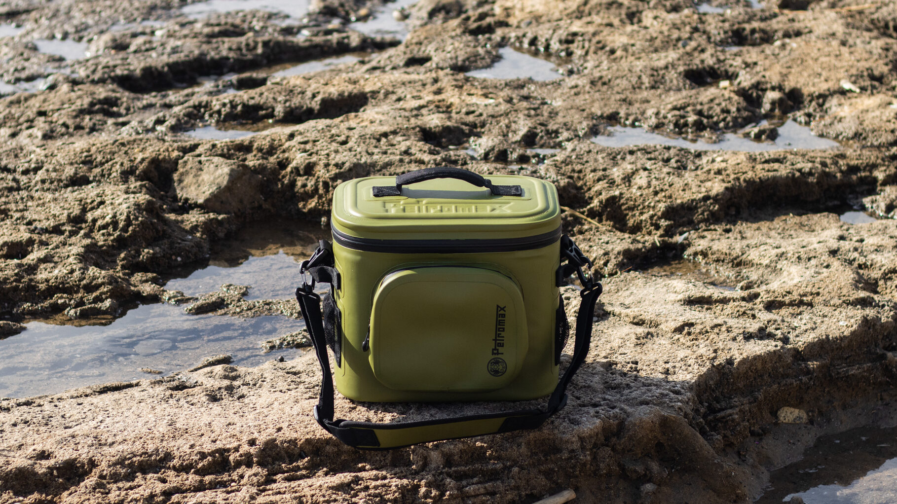 Medium size army green cooler on rocks at beach.