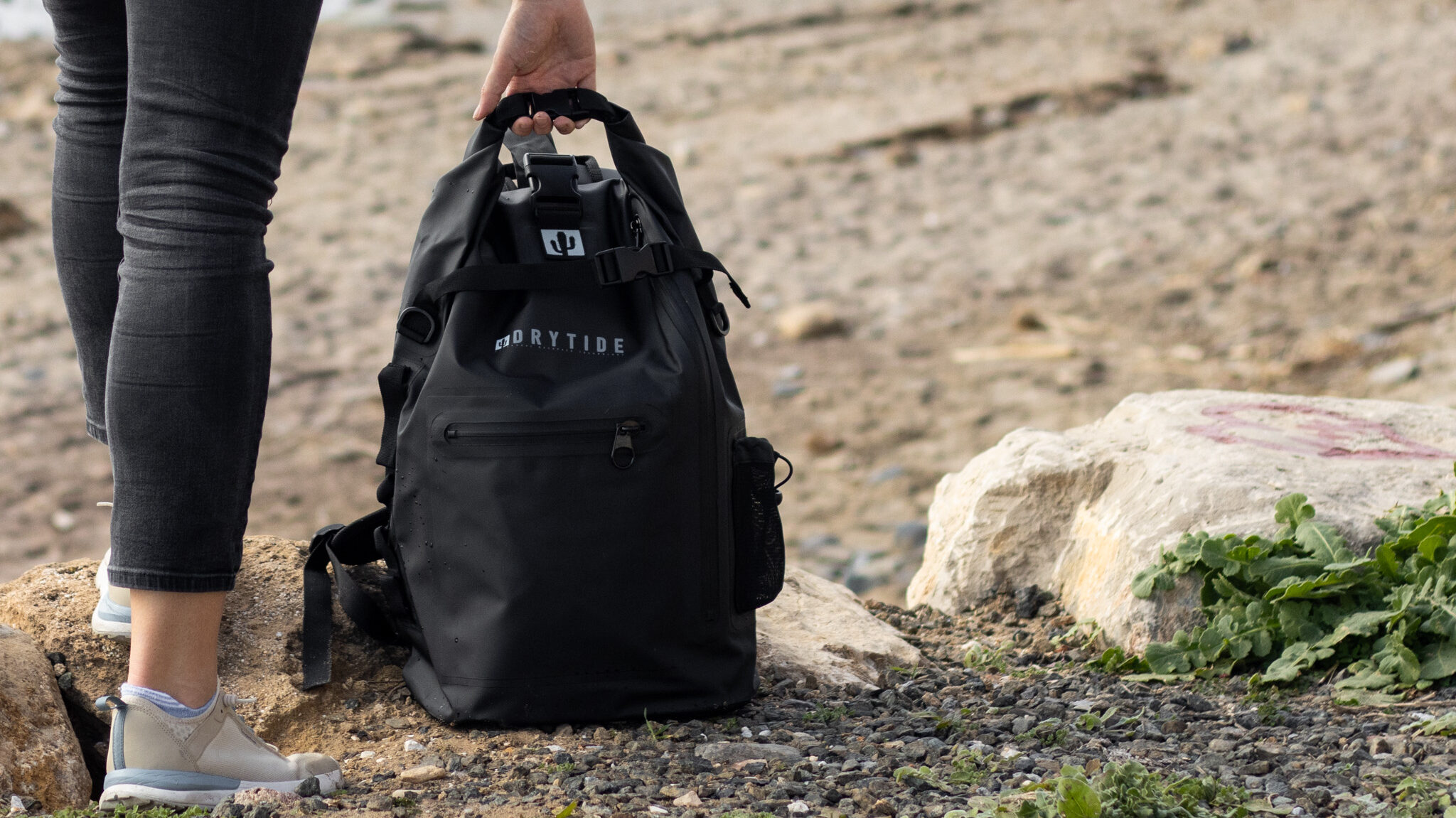 Black waterproof backpack on ground at beach.