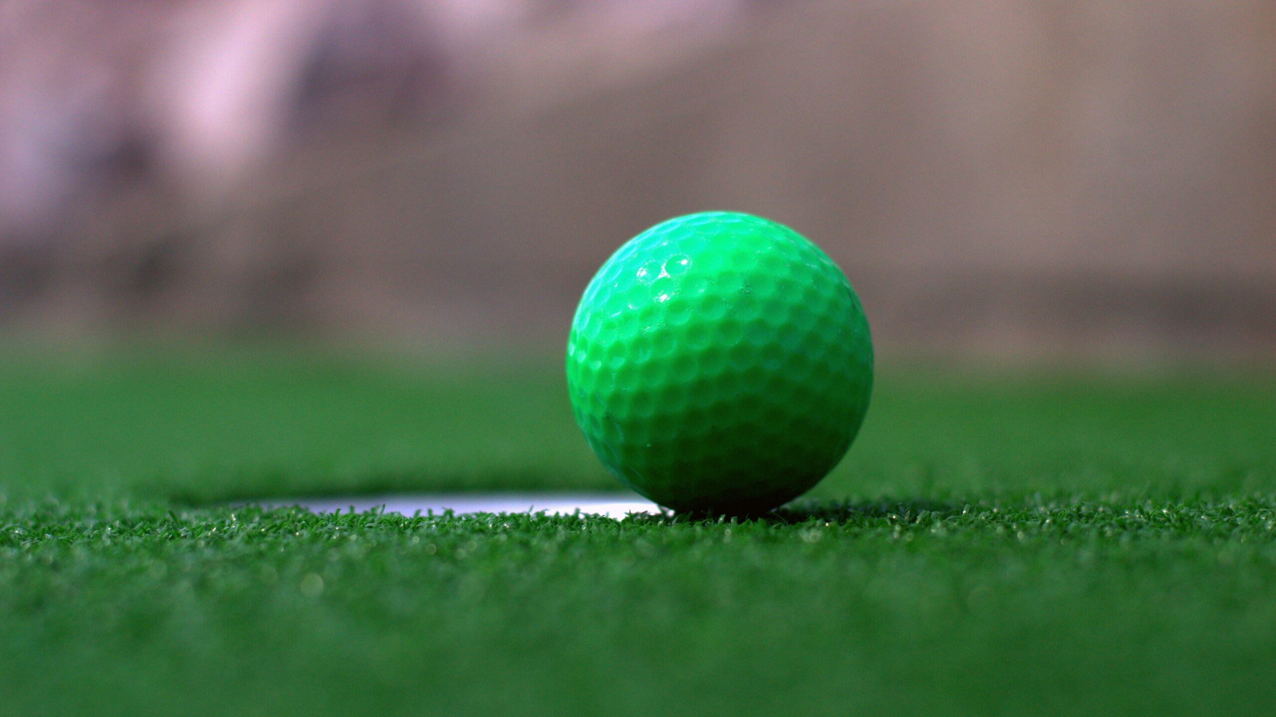 Green golf ball near hole at mini golf. 