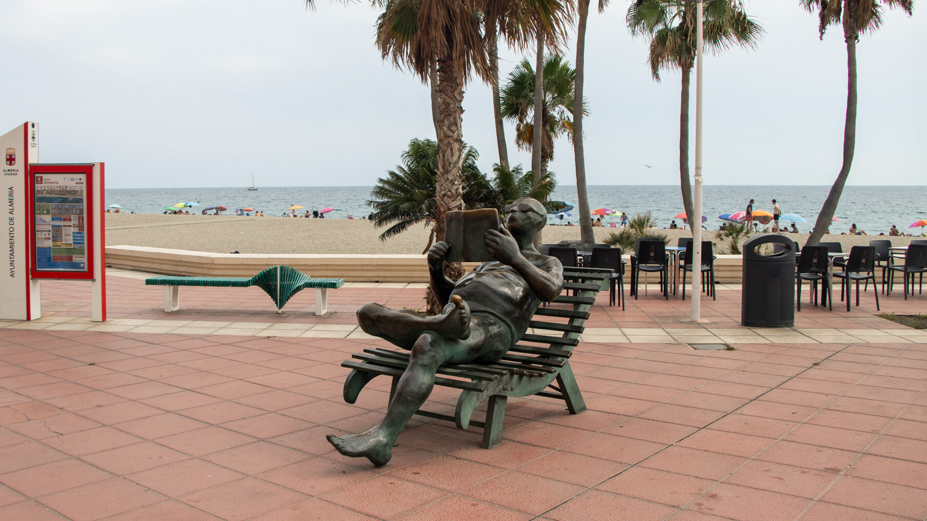 Statue of man sitting and reading along waterfront.