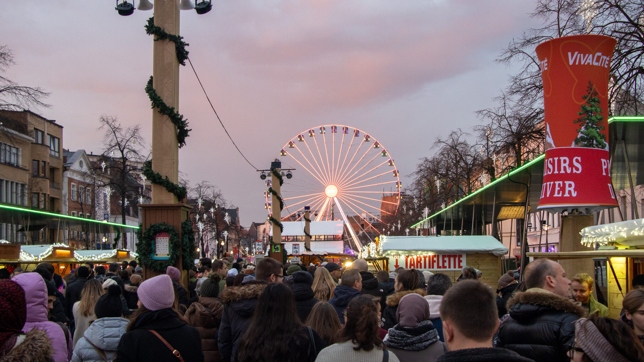 Christmas market with stalls and Ferris wheel at sunset.