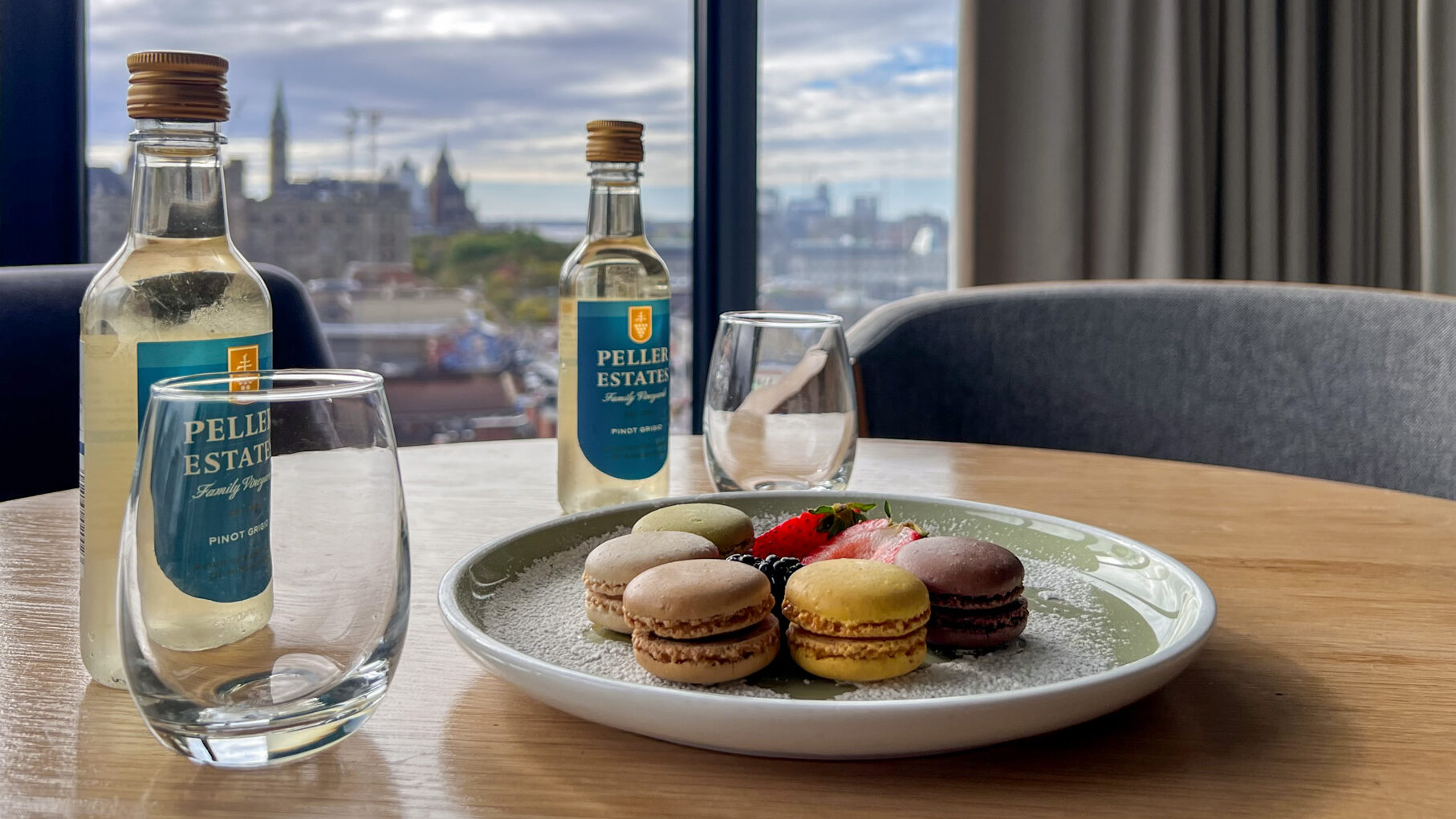 Andaz Ottawa | Krista the Explorer Macrons and two small bottles of wine at table in front of window.