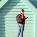 Blonde woman walking along pier with backpack on.