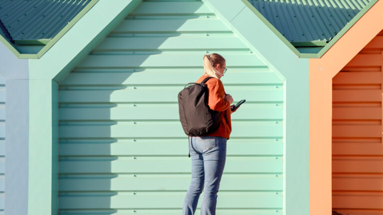 Blonde woman walking along pier with backpack on.