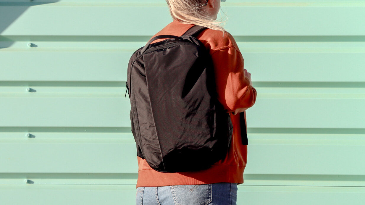 Amond Oaks Backpacks | Krista the Explorer Woman wearing a black backpack next to colourful hut.