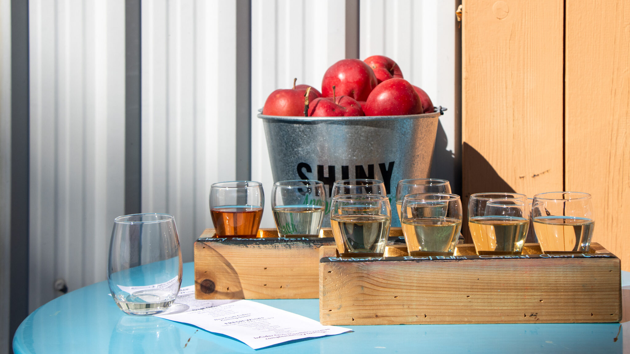 Shiny Apple Cider Winery | Krista the Explorer Flights of luxury apple cider on blue table outside.