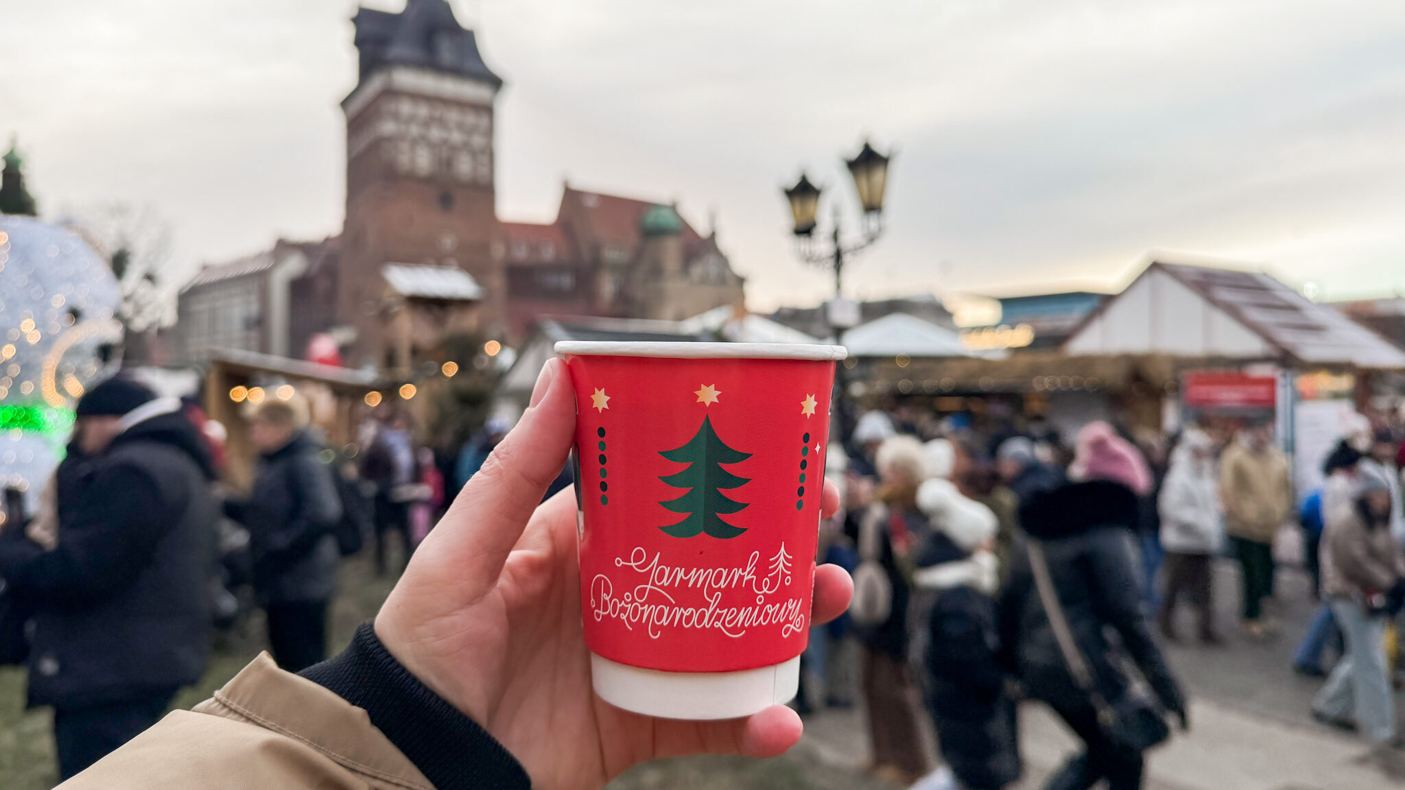 Person holding cup of hot chocolate at Christmas market.
