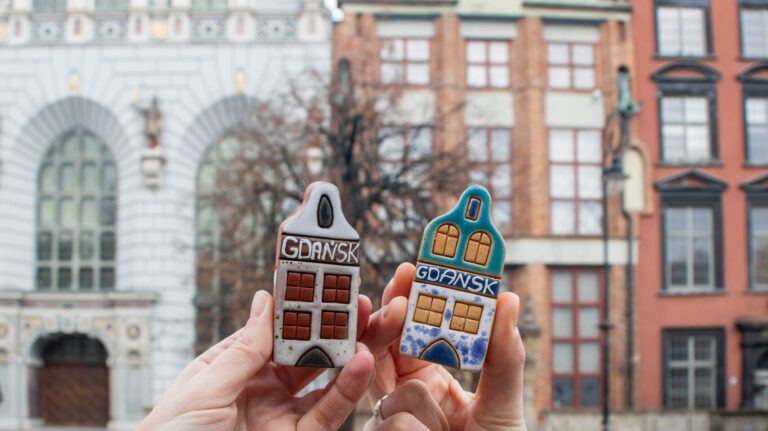 Two small ceramic Polish houses being held up.