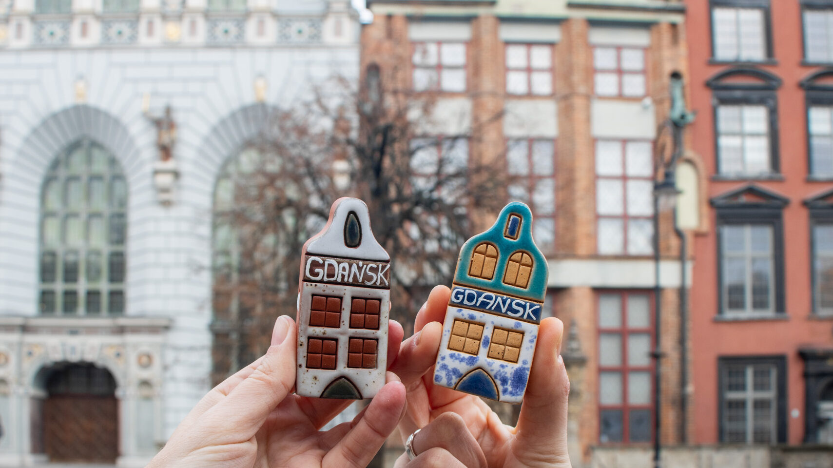 Two small ceramic Polish houses being held up.
