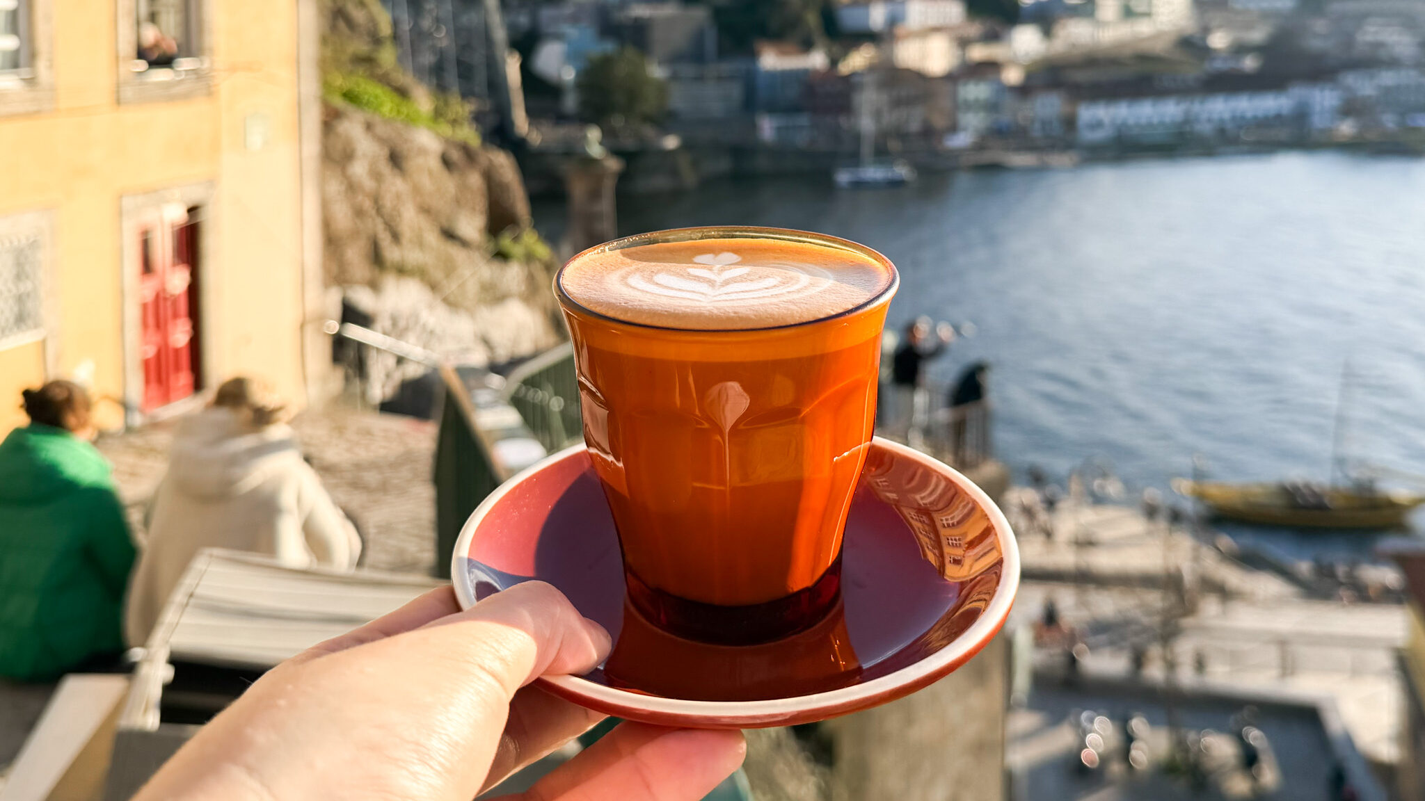 Latte on plate held up with view of Porto bridge.