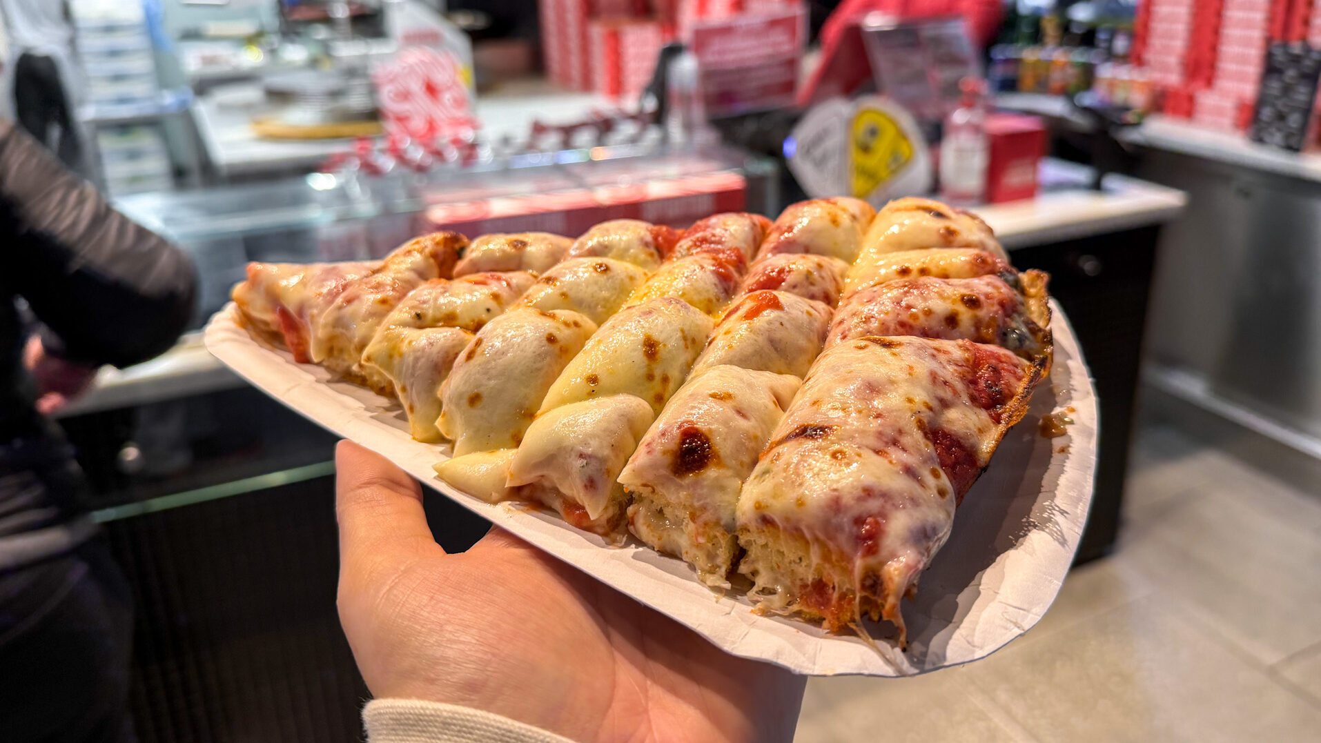 Large thick slice of margarita pizza on paper plate.