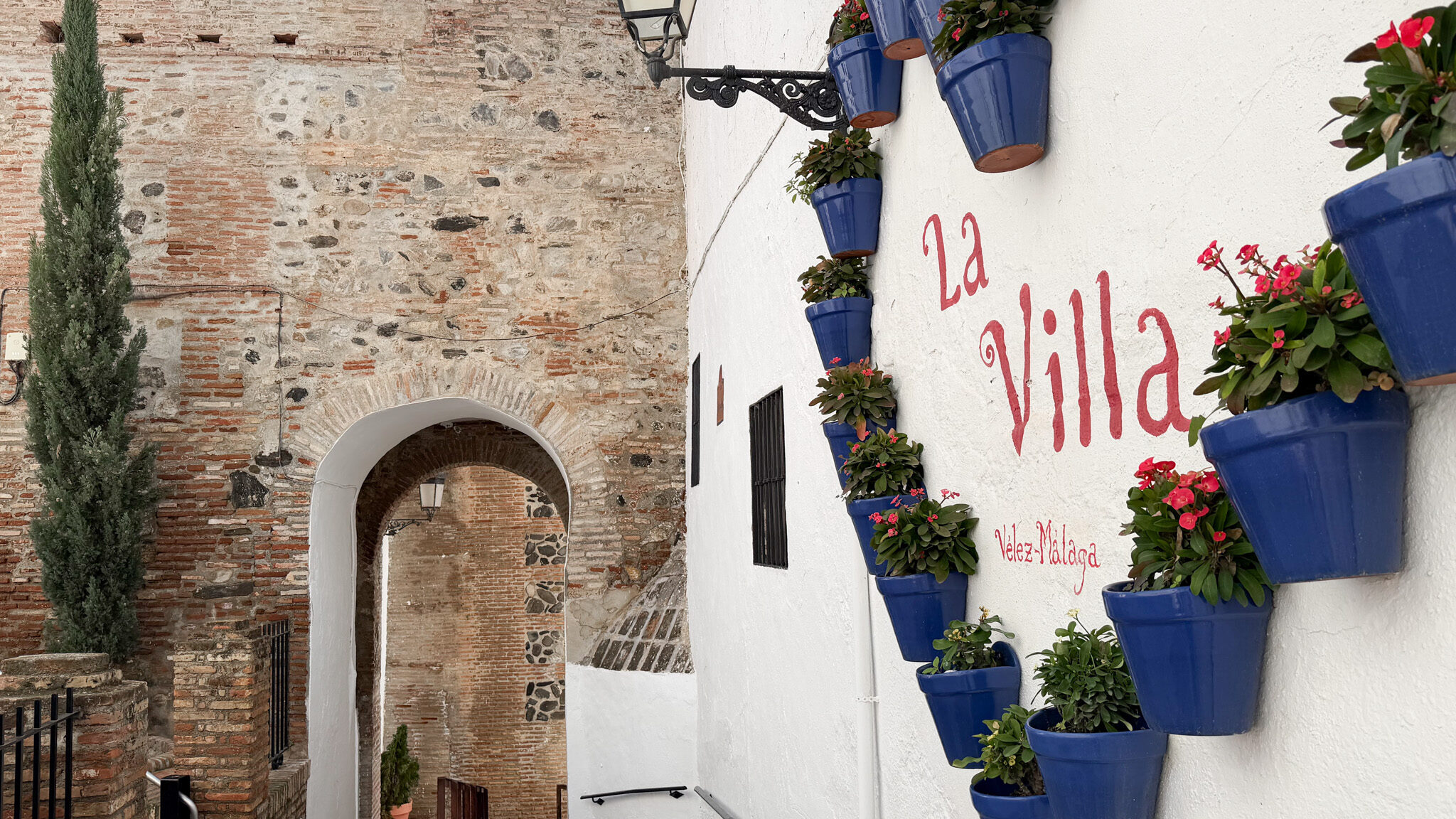 Puerta Real de la Villa Velez Malaga | Krista the Explorer Historic arch next to whitewashed wall with flower pots.