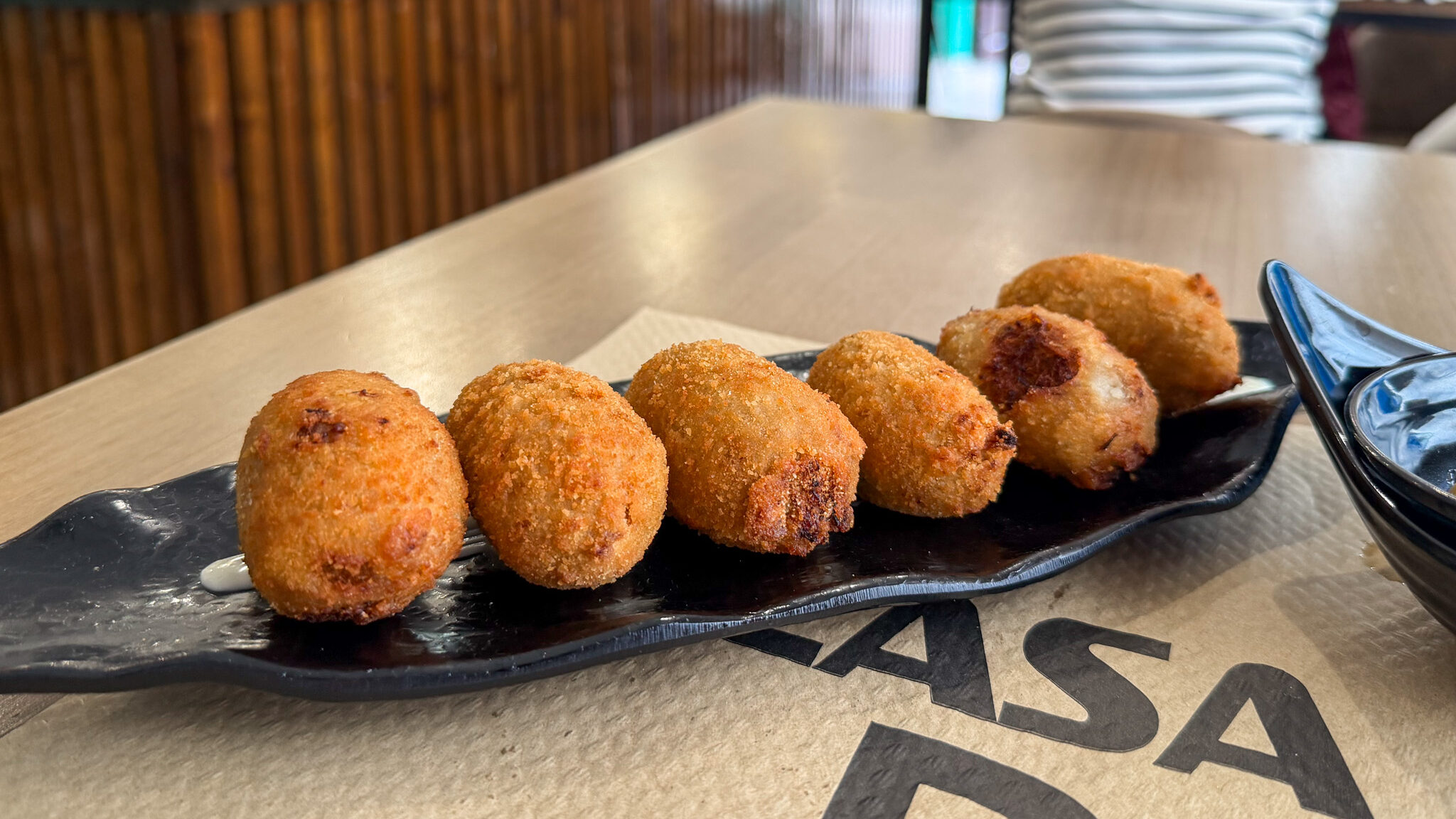 Casa Domi Velez Malaga | Krista the Explorer Black plate with fresh croquettes in a line.