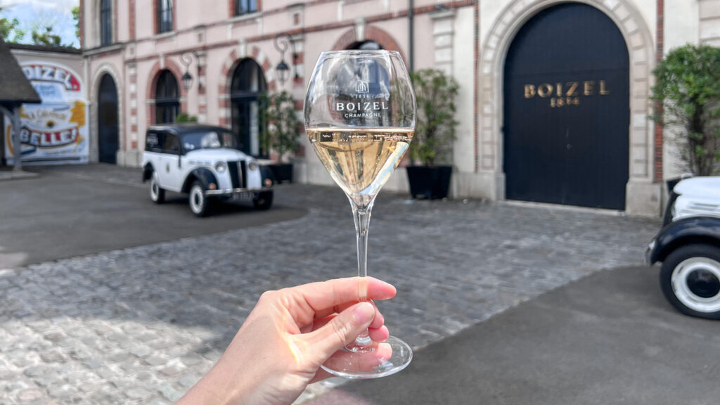 Glass of champagne held up in front of historic house.