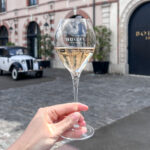 Glass of champagne held up in front of historic house.