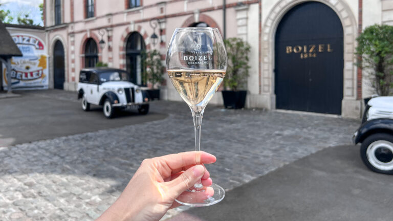 Glass of champagne held up in front of historic house.
