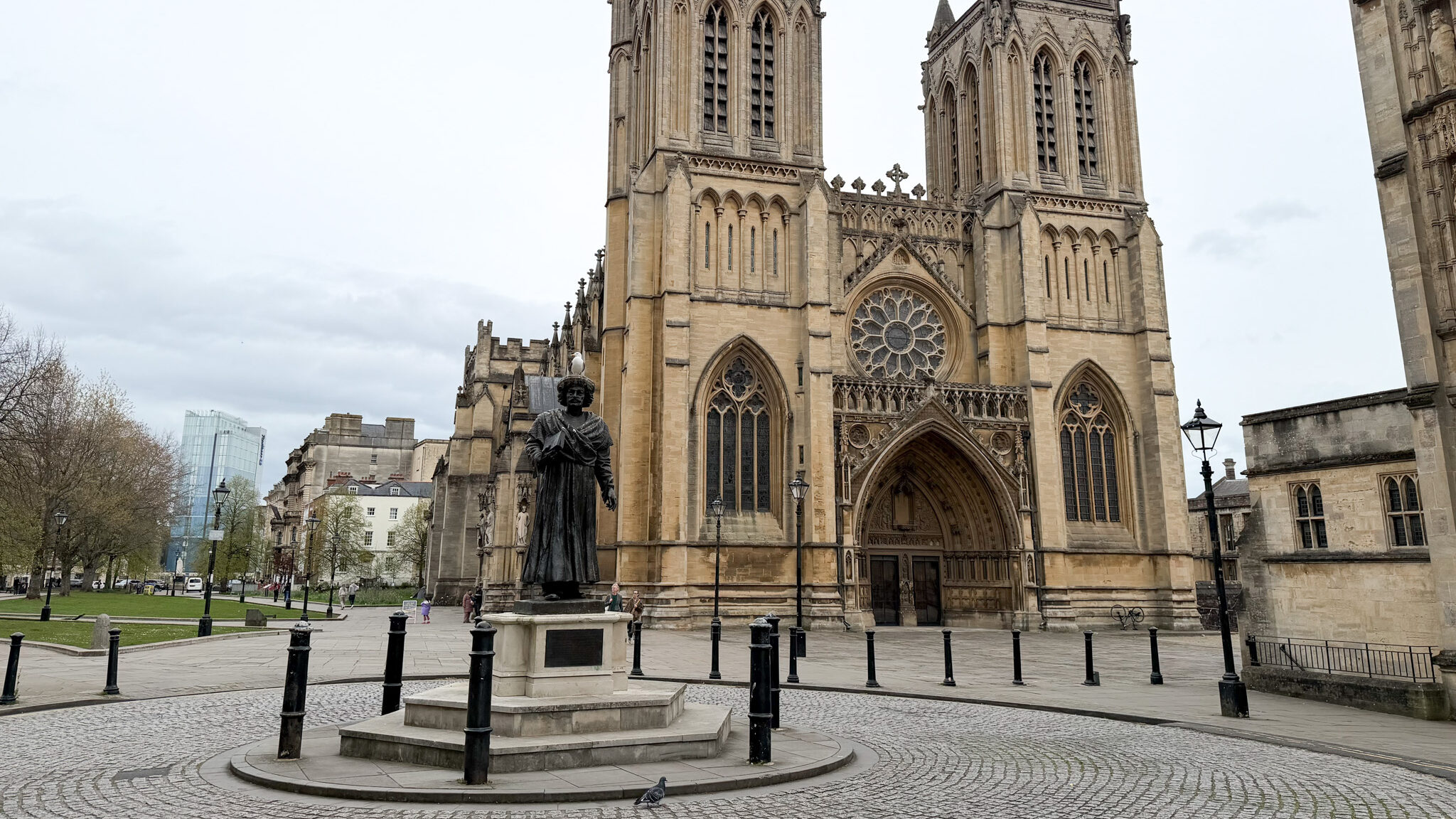 Front view of a Gothic cathedral with twin towers, ornate stone carvings, and a statue in a square foreground in Bristol.