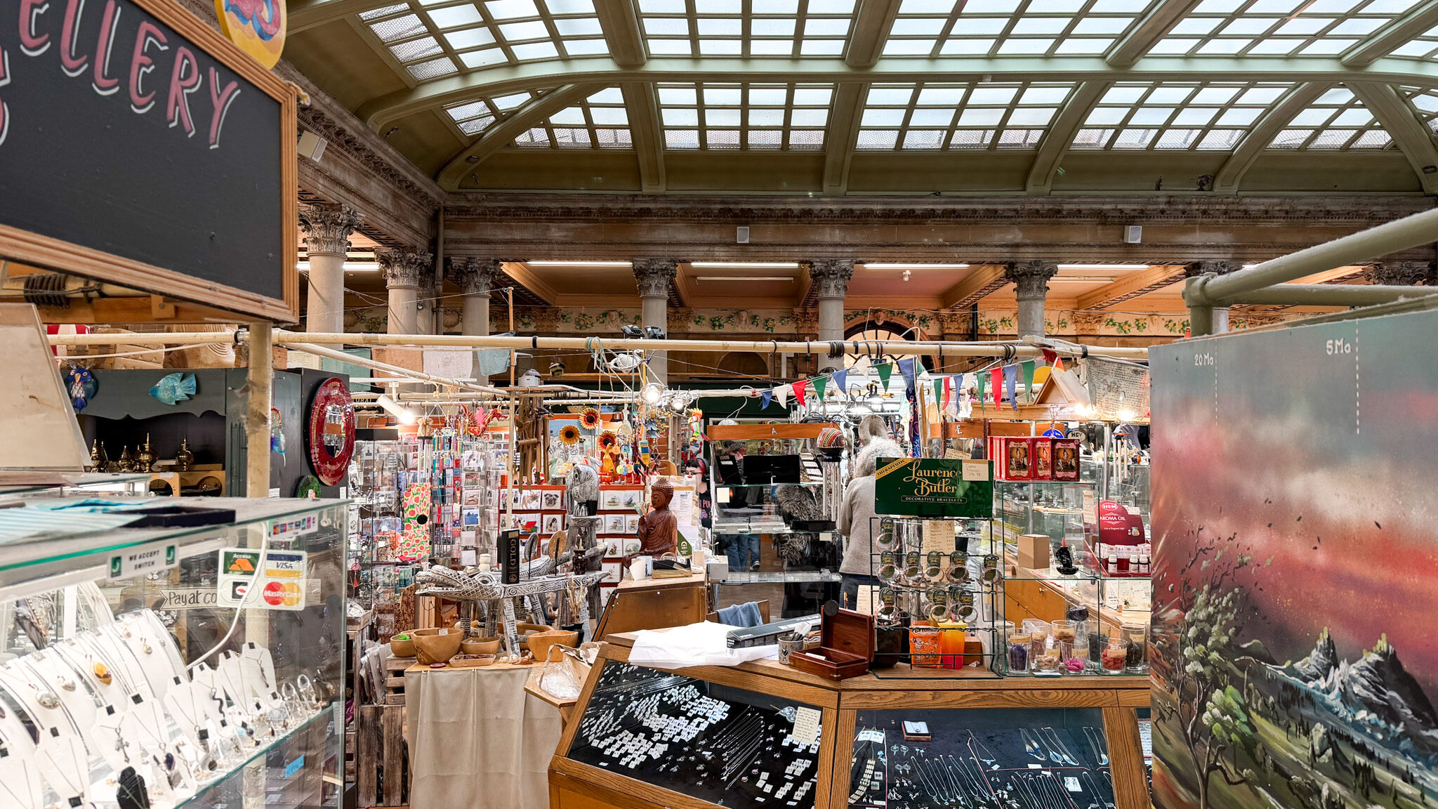 Indoor market stall with glass display cases under a large glass skylight archive ceiling.