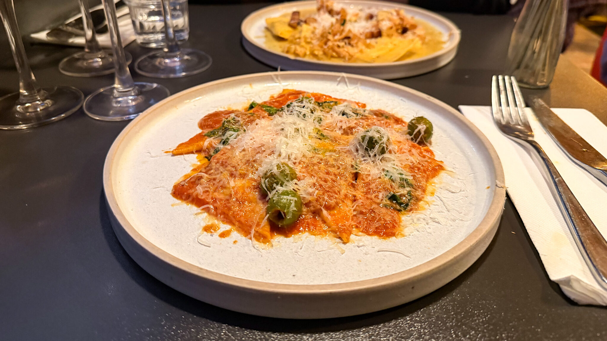 Plate of pizza with tomato sauce, basil, and grated cheese on a dark table.