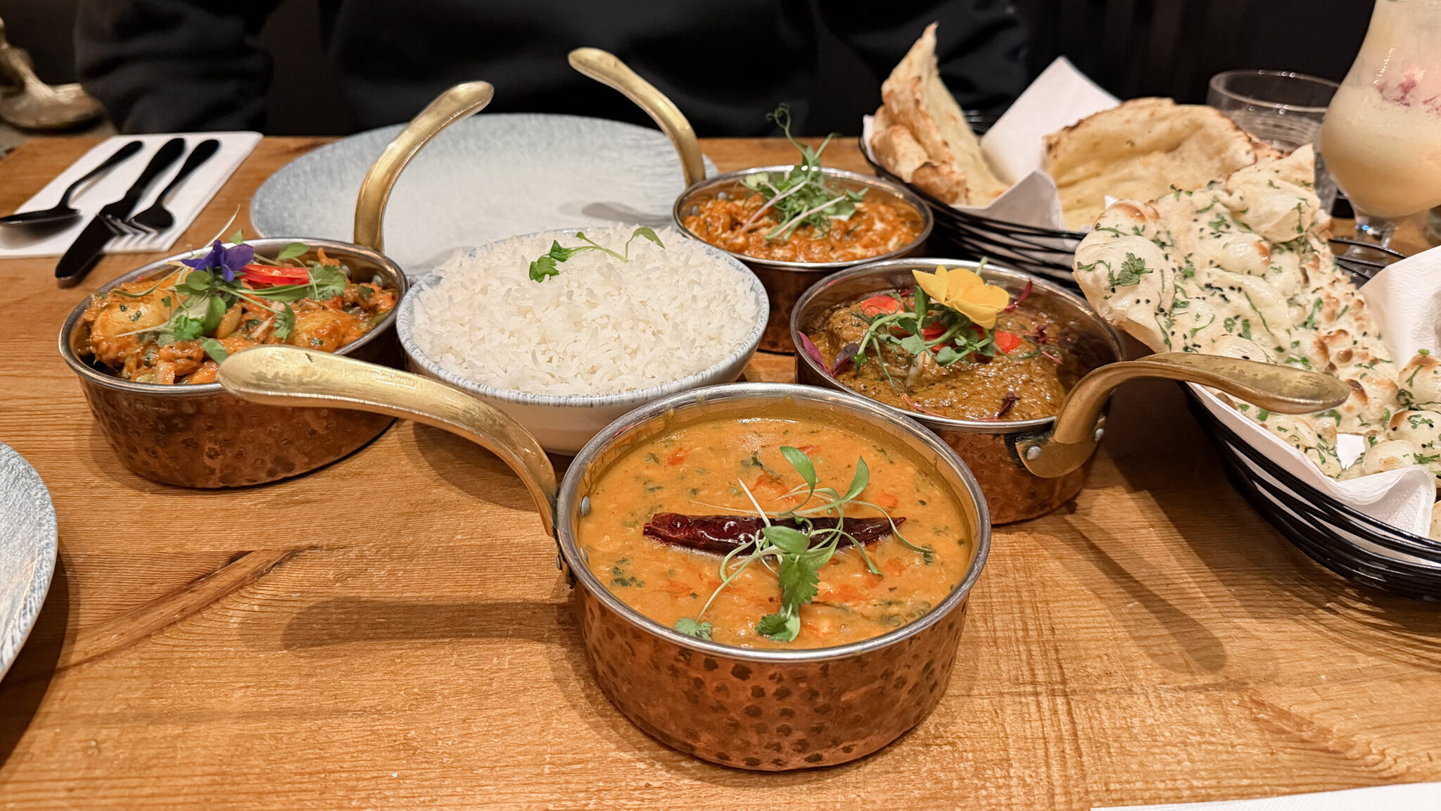 Copper serving bowls hold multiple curries with fresh herbs.